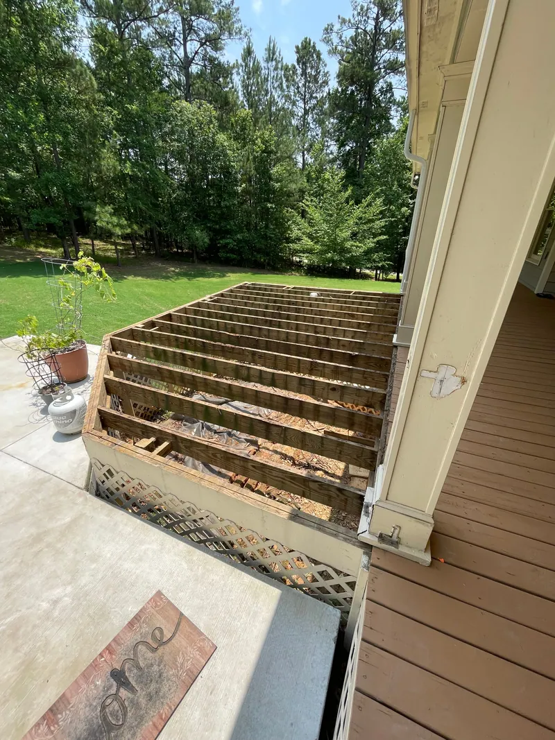 The same deck stripped to bare framing with every floorboard gone, showing the joists, the lattice skirting below and the concrete patio alongside.