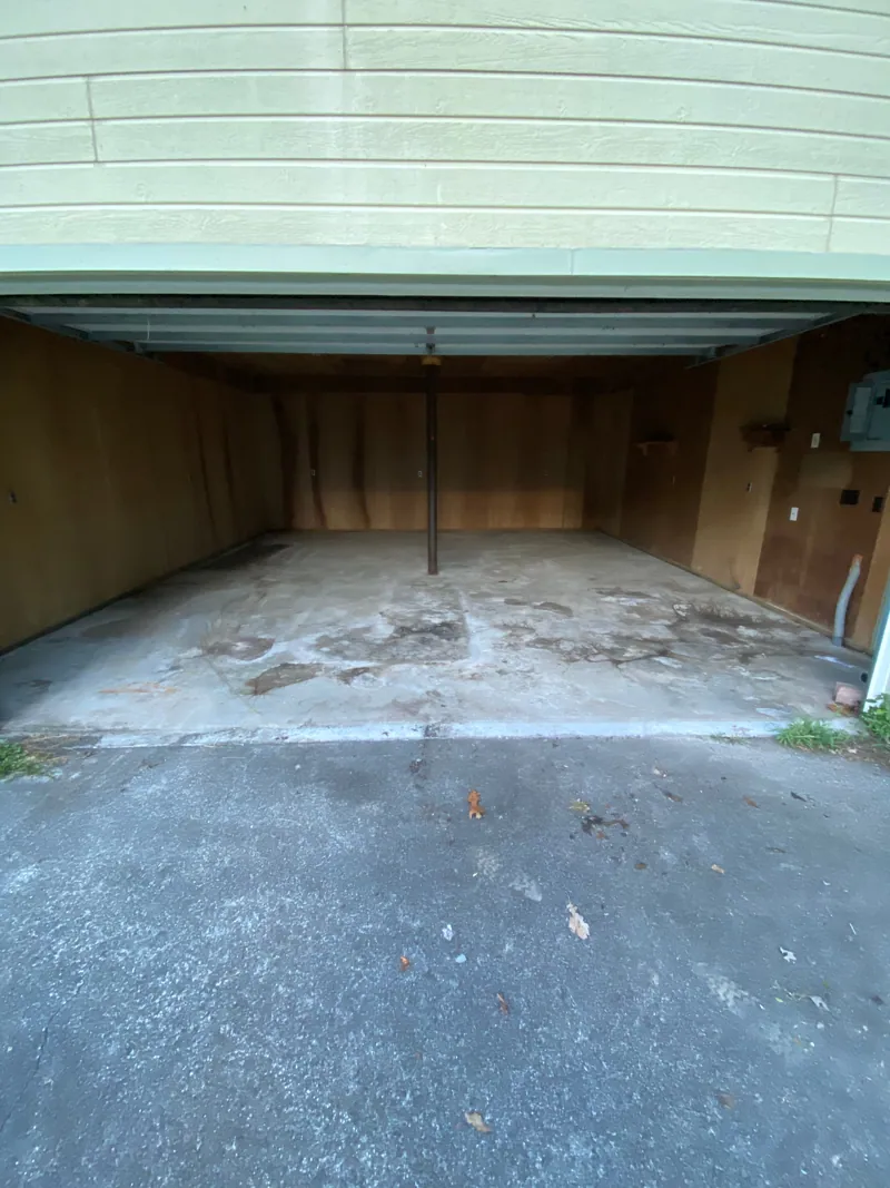 The same garage cleared to an empty concrete floor, with the door raised to the driveway and nothing left but the support post and the paneled walls.